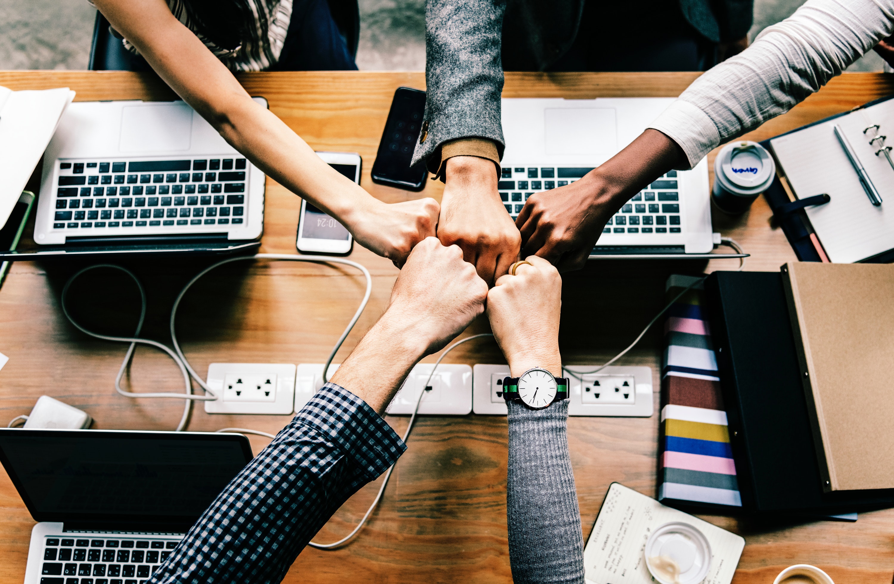 A circle of people on laptops putting their hands together