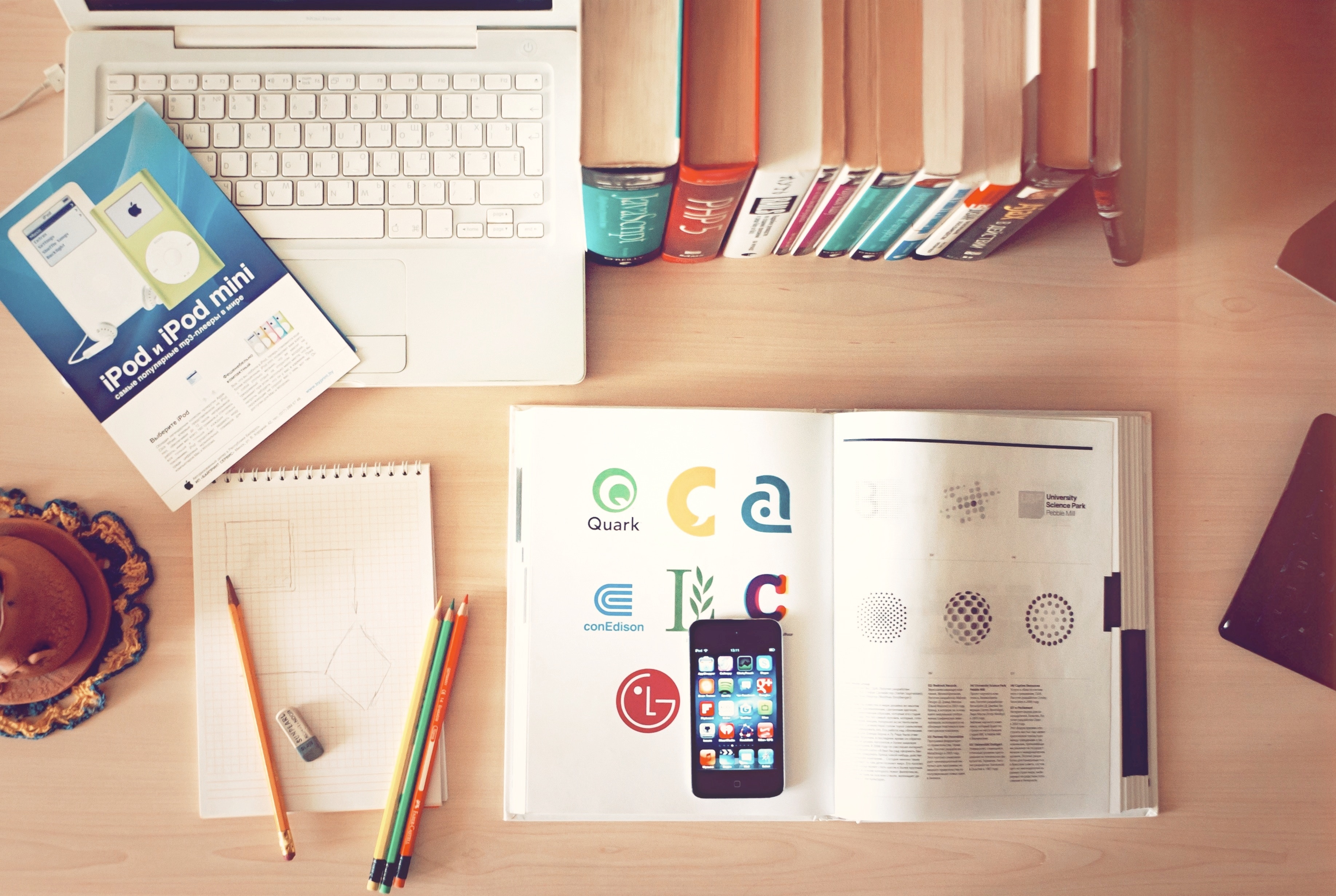 A desk with a laptop, sketch books, and a mobile device