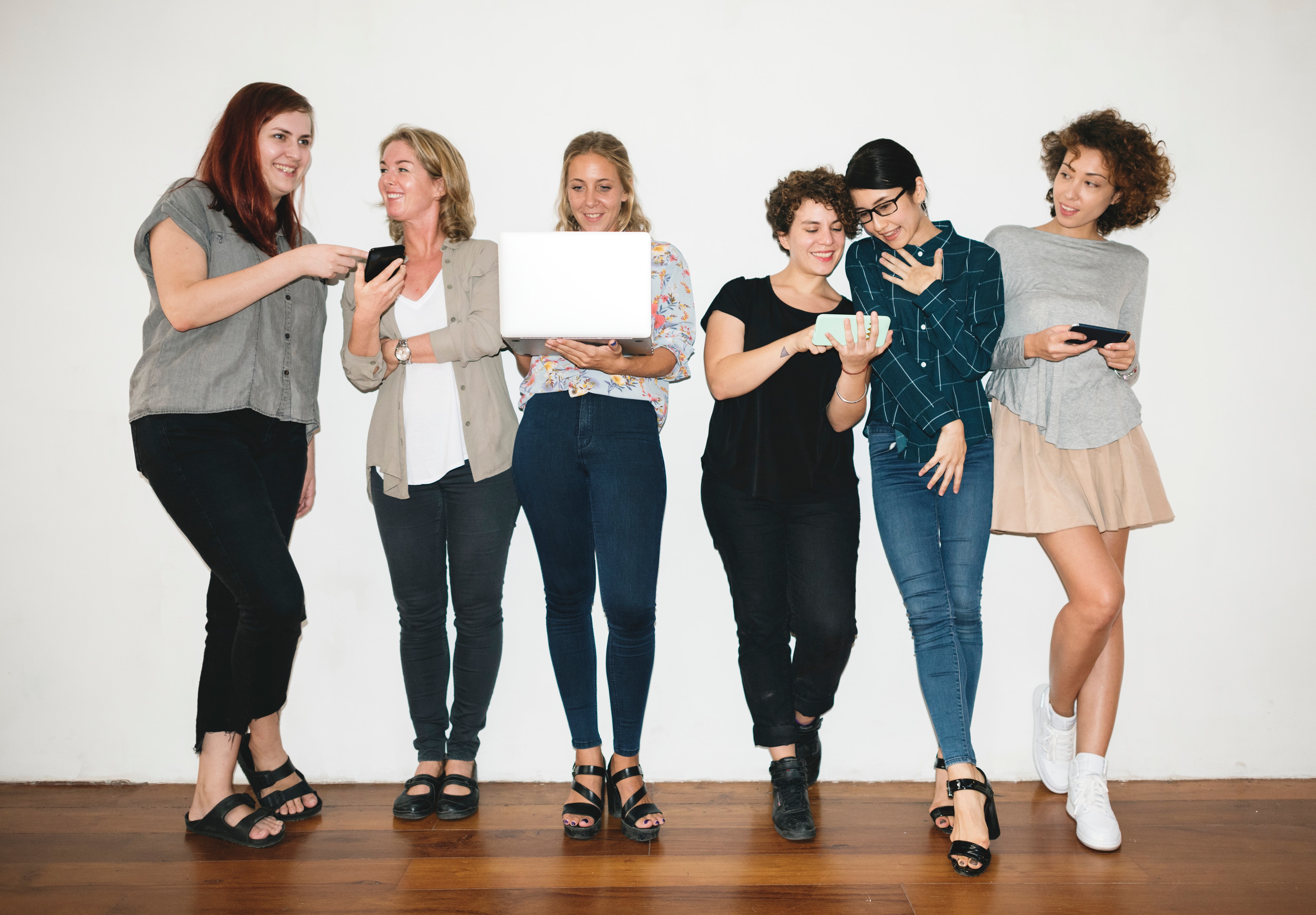 A group of women standing against a wall, holding laptops